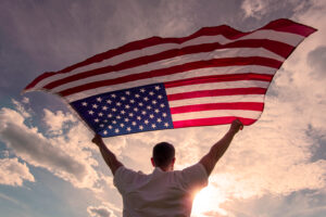 A man holding an american flag in front of the sun.