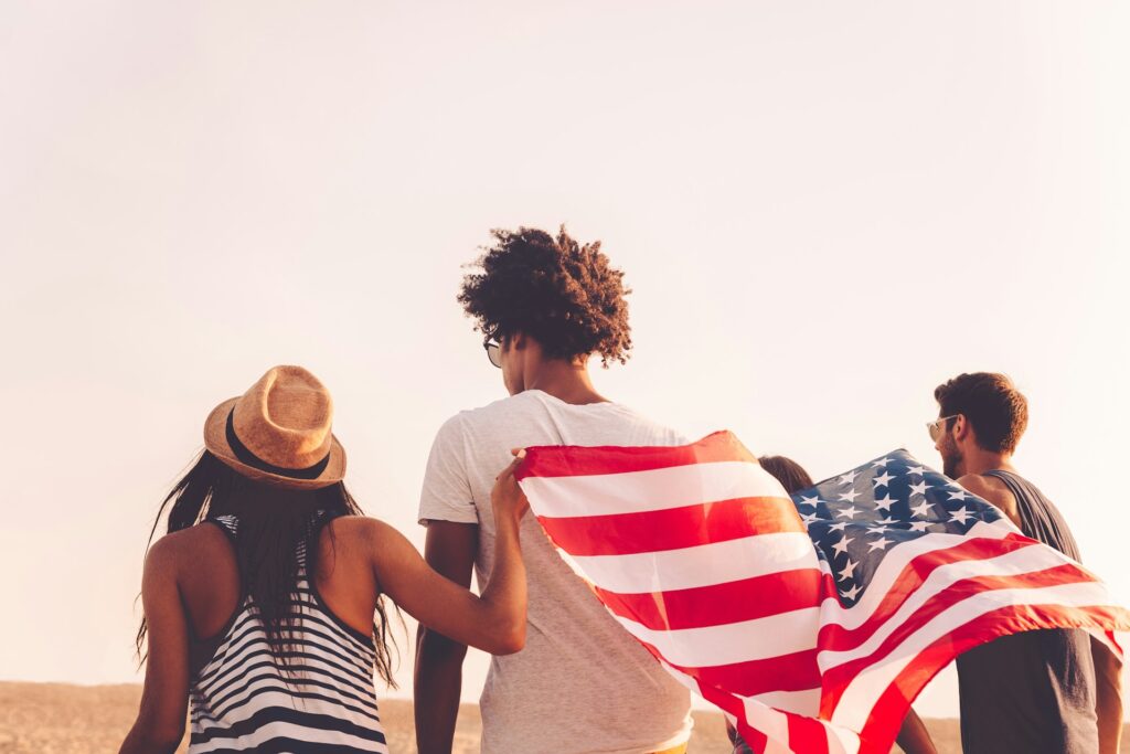 A group of friends with an American flag, enjoying a sunny day outdoors.